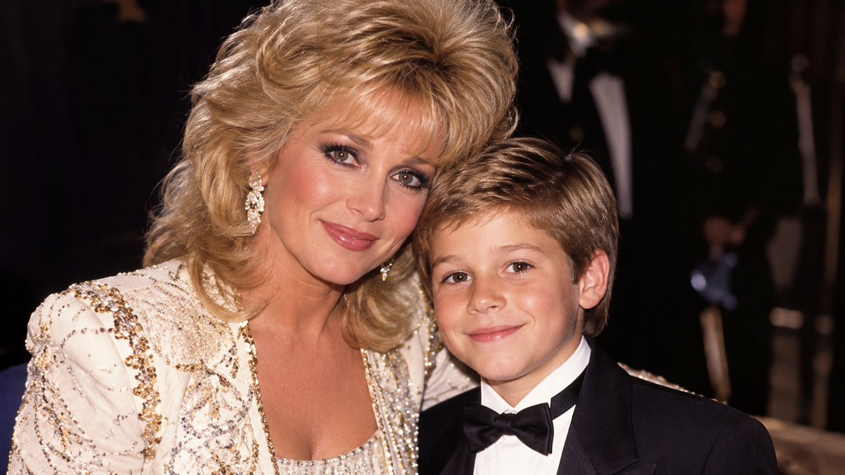 Barbara Mandrell posing with a young boy at a formal event.